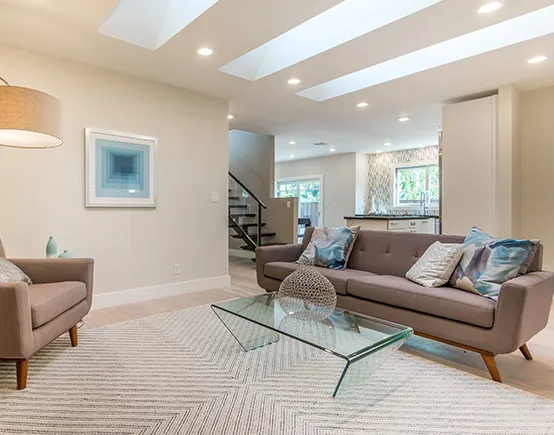 A modern living room with a glass coffee table, a gray sofa, and a patterned rug.