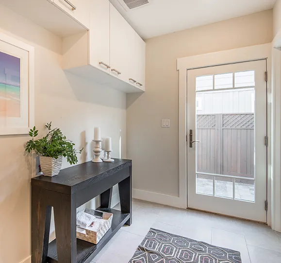 A small entryway with a black console table, a potted plant, and wall-mounted cabinets. A white door with a glass pane leads to the backyard.